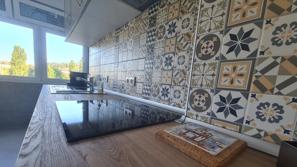 A modern kitchen with a long countertop, a sink, and a backsplash with patterned tiles. - Lisbon Metro Yellow Line (Loures)