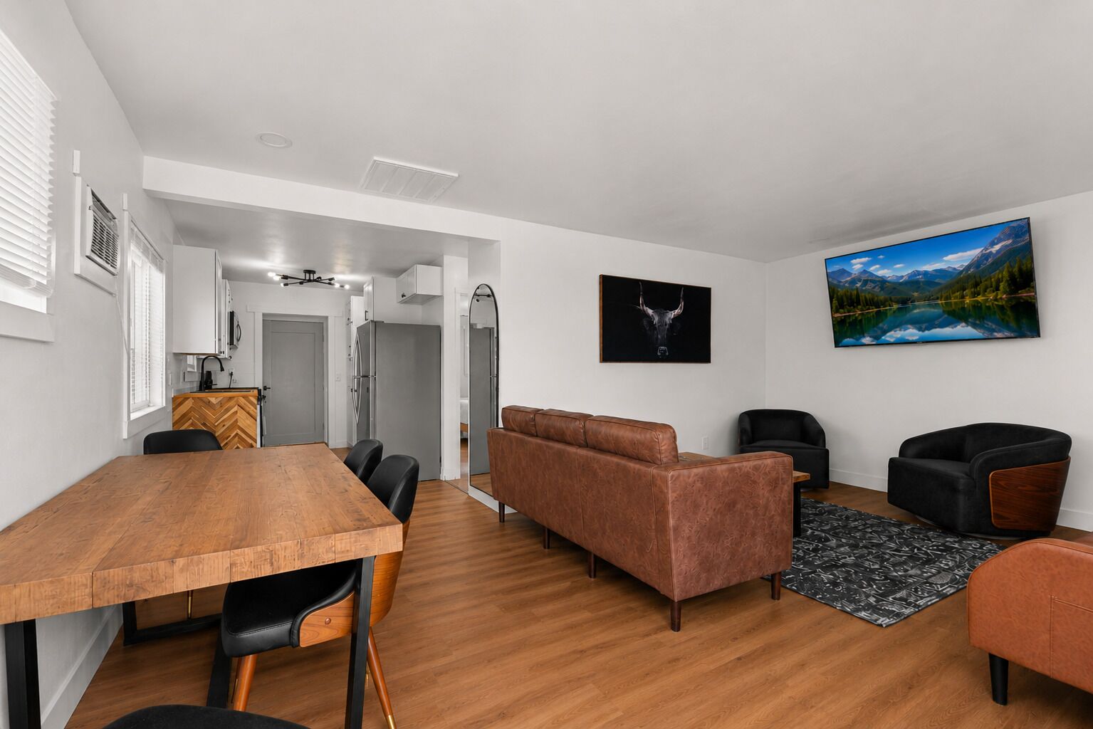 Una sala de estar moderna con una mesa de comedor de madera, sofás de cuero y un cuadro grande de un paisaje.