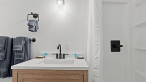 A bathroom with a white sink, wooden cabinet, towel rack, and a light fixture.