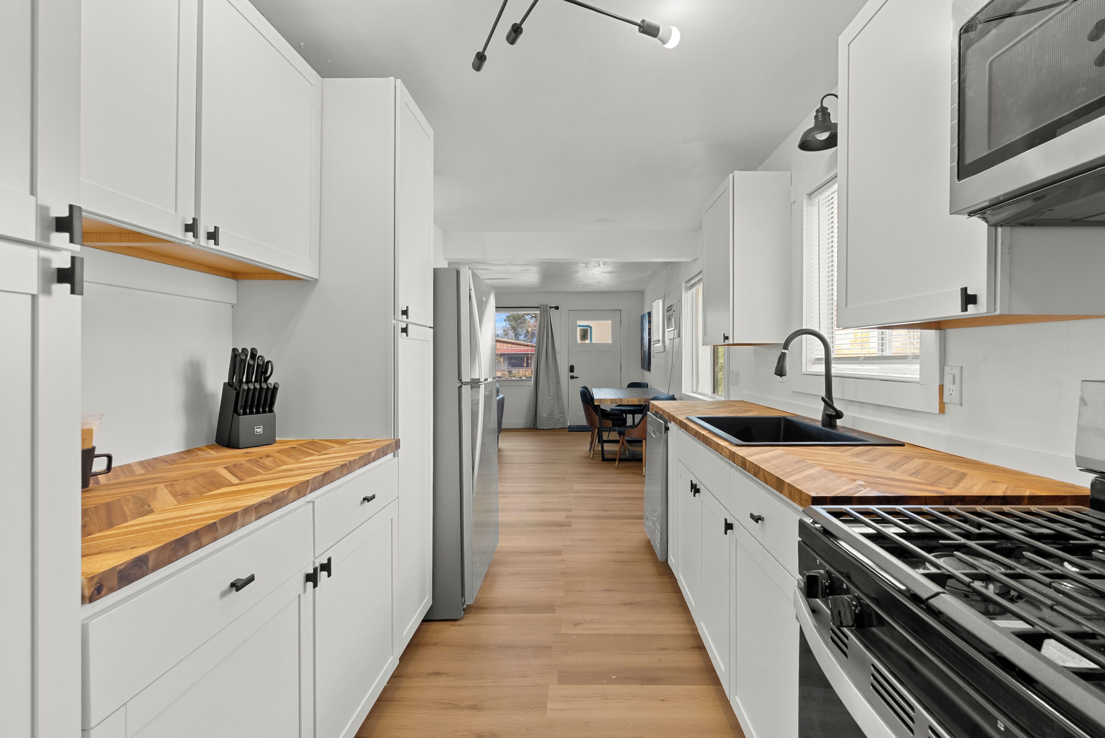Cocina moderna con armarios blancos, encimera de madera, estufa y un área de comedor al fondo.