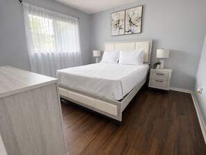 A bedroom with a bed, bedside tables, a nightstand, a window with sheer curtains, and two wall-mounted flower paintings. - Coastal Getaway in Apollo Beach/ Pet Friendly ! (Apollo Beach)
