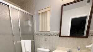 Een badkamer met douche, toilet, wastafel en spiegel.