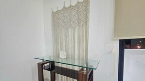 Un tavolo con piano in vetro e gambe scure, un elemento decorativo a parete e una porta con interruttore della luce.