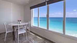 Una habitación con una mesa de comedor, sillas, un florero con flores y un ventanal con vista al océano.