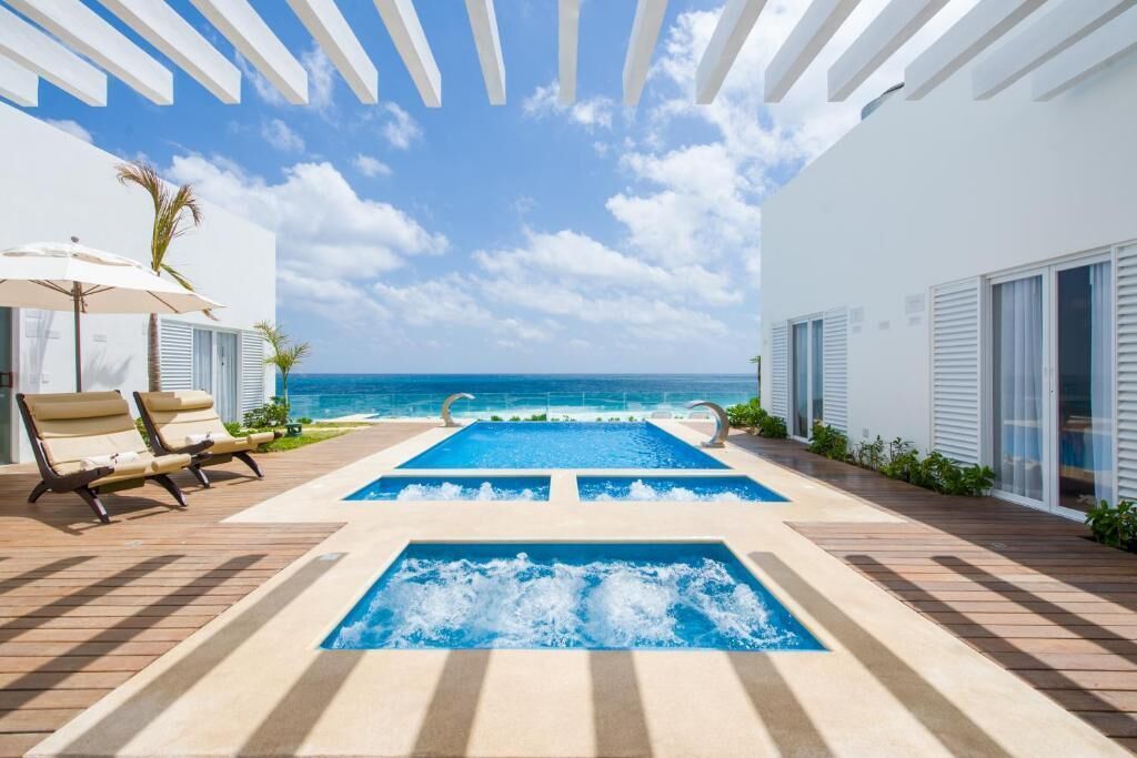 Un espace piscine agrémenté de deux bassins rectangulaires, de chaises longues et offrant une vue sur l’océan.