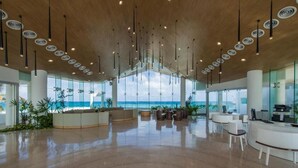 Un vestíbulo espacioso con techo alto, iluminación colgante moderna, una recepción y vistas al océano.