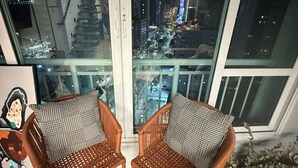 A balcony with two wicker chairs, a view of a cityscape at night, and a large window. - Beira Mar Ocean-View Loft — Steps from Meireles & Iracema Beach (Fortaleza)