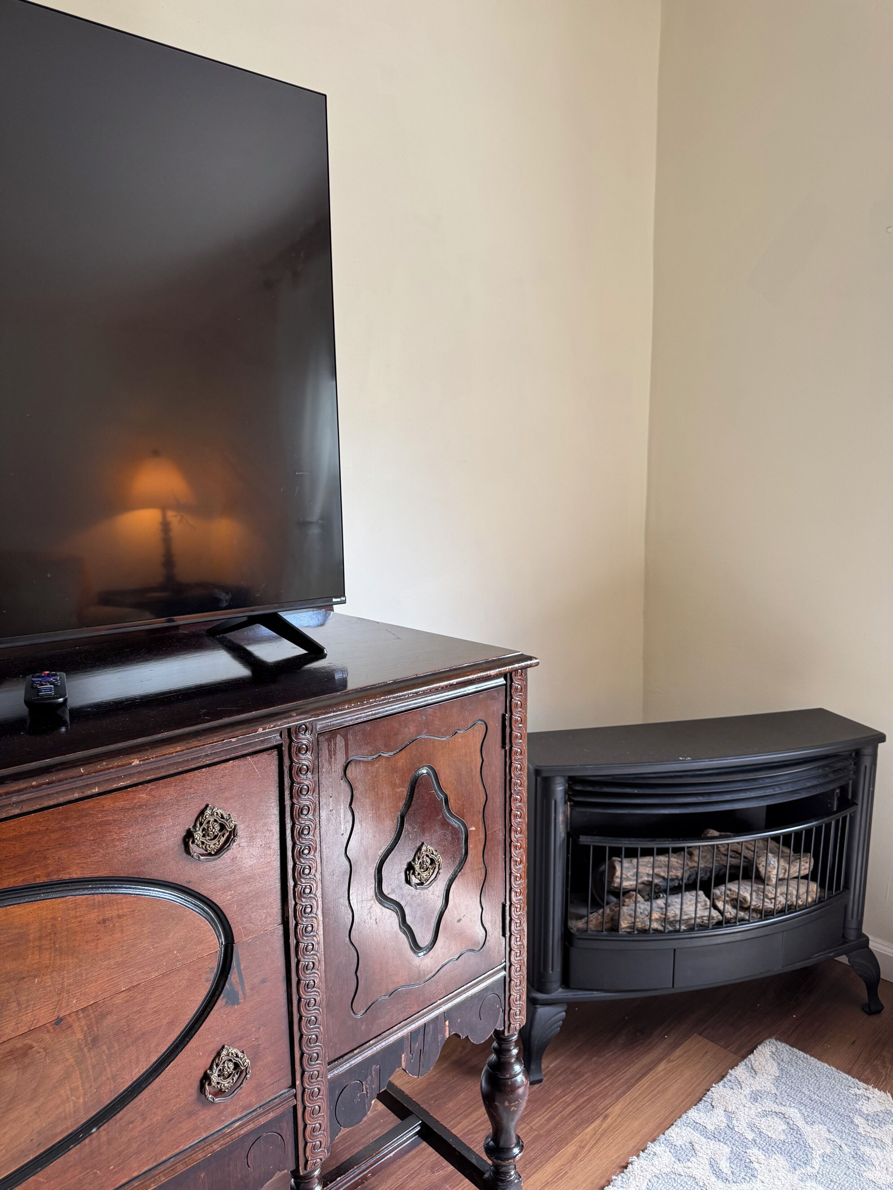 Un comò in legno con una TV a schermo piatto sopra, un mobile decorativo con intagli elaborati e un camino nero con legna.