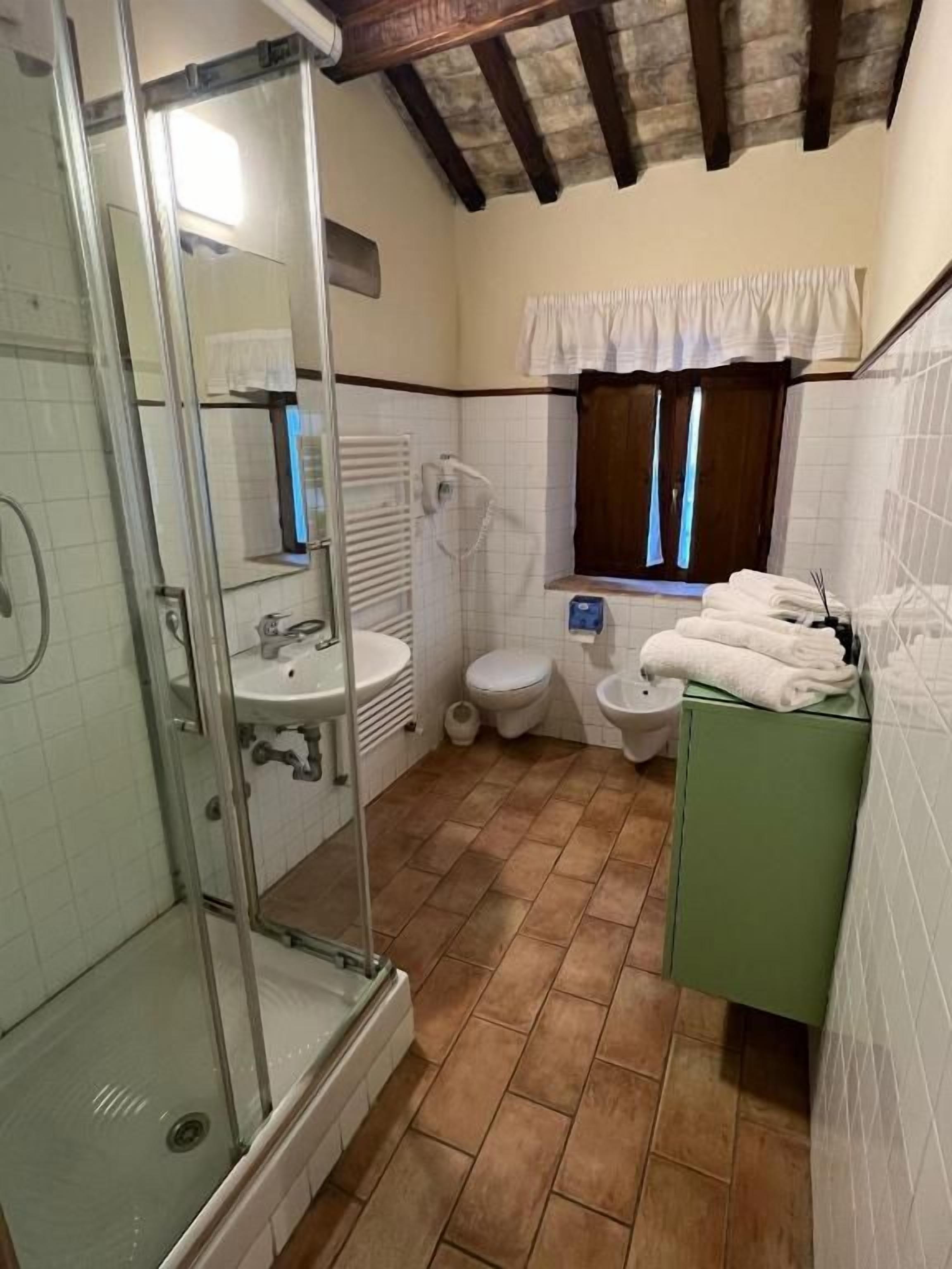 Un bagno con box doccia in vetro, un water, un lavandino e una finestra con tende.