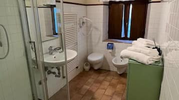 Un bagno con box doccia in vetro, un water, un lavandino e una finestra con tende.