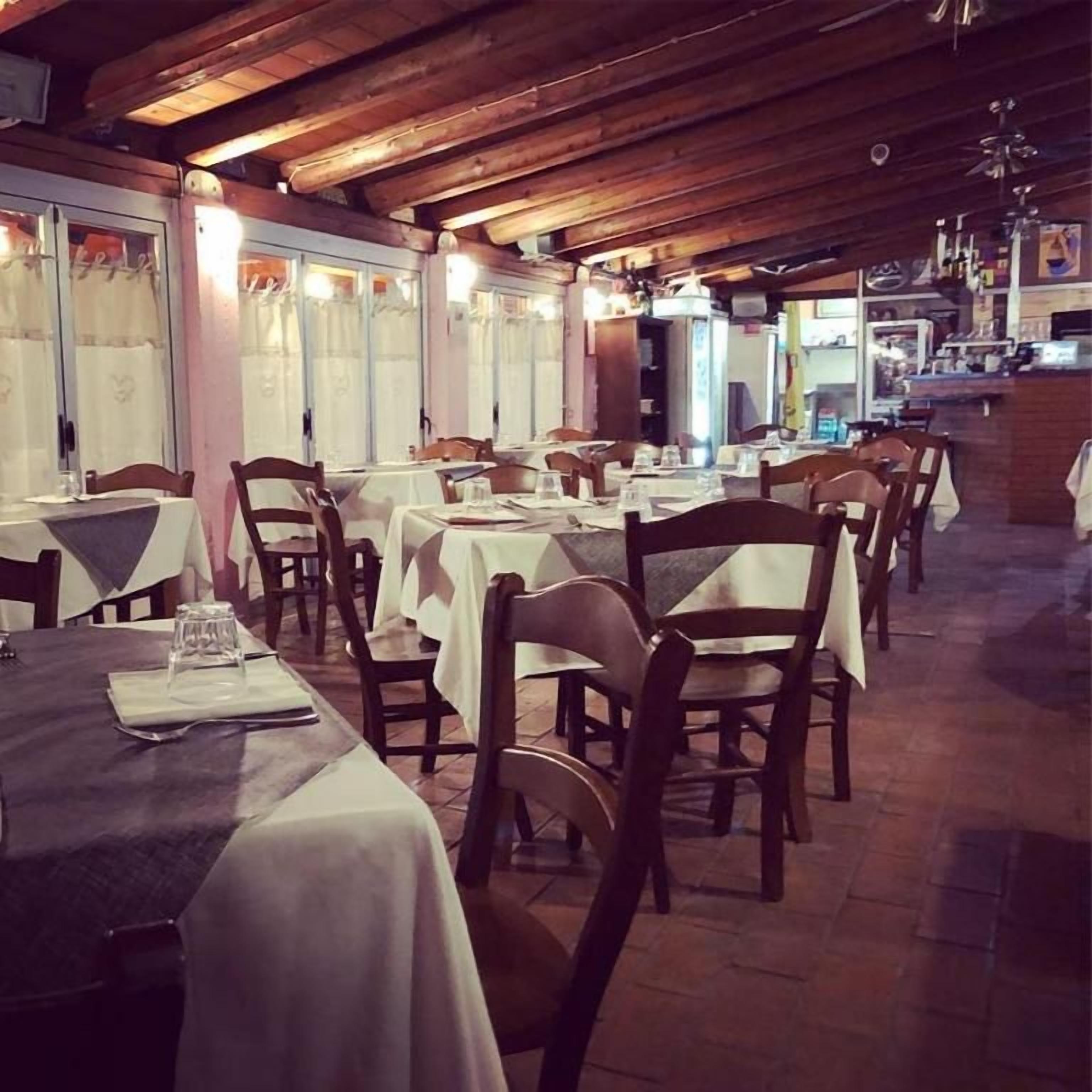 Un ristorante con travi in legno, tavoli con tovaglie bianche e sedie.