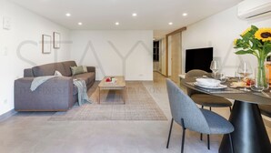 En moderne stue med sofa, sofabord og spiseområde med stole og et bord dækket til et måltid.