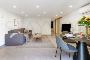 Ein modernes Wohnzimmer mit Sofa, Couchtisch und Essbereich mit Stühlen und Tisch, gedeckt für eine Mahlzeit.