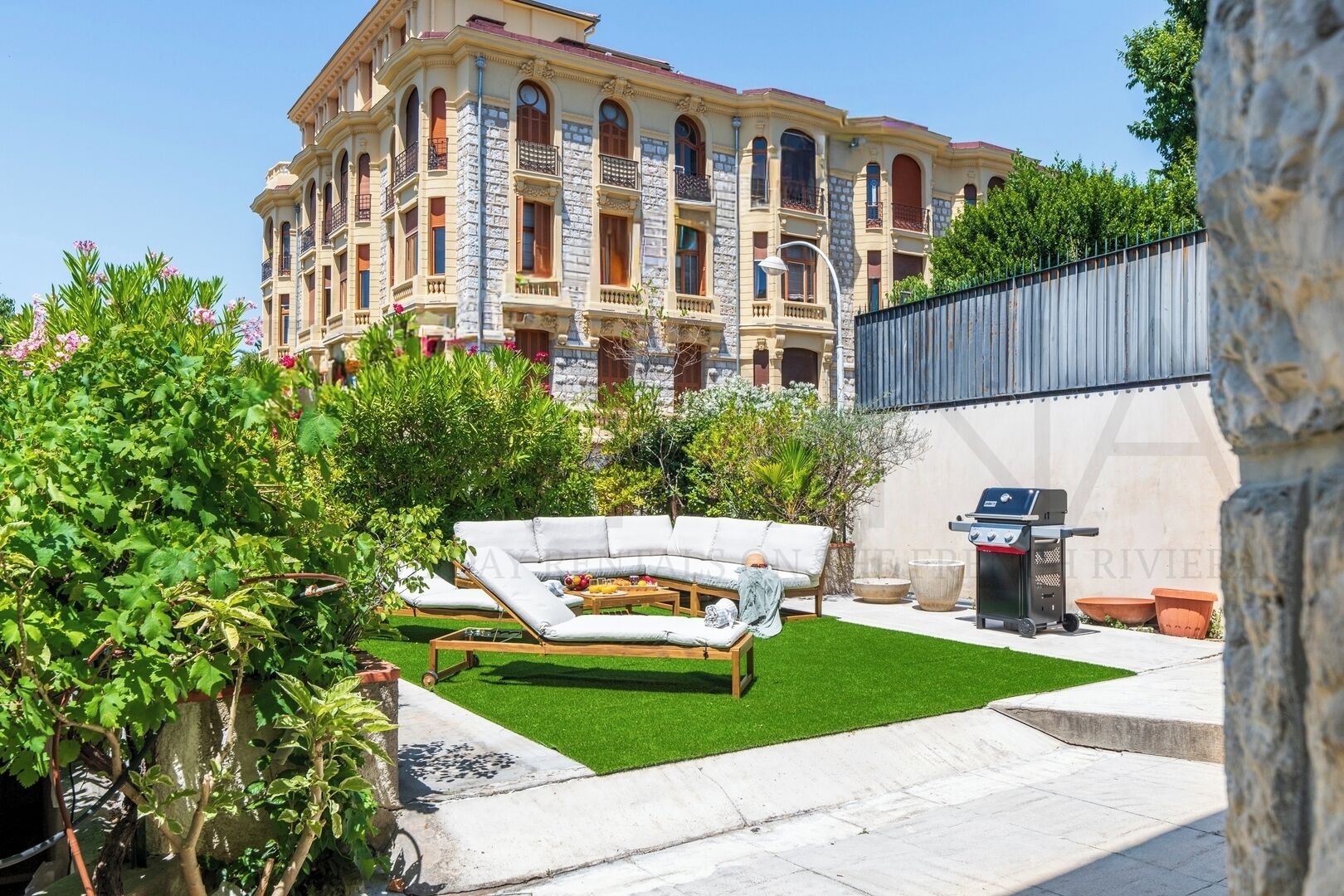 Ein Innenhof mit einer weißen Couch, einem Grill und einem großen Gebäude im Hintergrund.