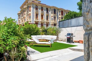 Ein Innenhof mit einer weißen Couch, einem Grill und einem großen Gebäude im Hintergrund.