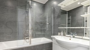 A modern bathroom with a glass-enclosed shower, a white sink, and a large mirror. - Déroulède (Nice)