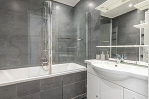 Ein modernes Badezimmer mit einer gläsernen Dusche, einem weißen Waschbecken und einem großen Spiegel.