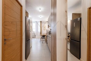 A narrow hallway with wooden doors, a kitchen area with a dining table and chairs, and a refrigerator. - Iris 1 bedroom apartment (Nice)