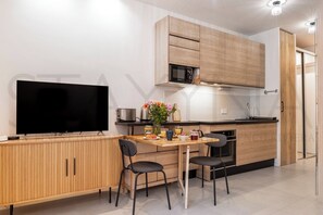 A modern kitchen with a flat-screen TV, wooden cabinets, a microwave, and a dining area with chairs. - Iris 1 bedroom apartment (Nice)