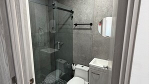 Et moderne badeværelse med en glasbrusekabine, et hvidt toilet og en vask med et spejl over.