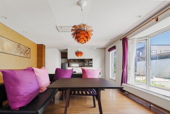 A modern living room with a dining table, purple cushions, and a hanging orange pendant light.