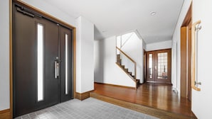 Un couloir avec une porte sombre, un escalier et un sol carrelé.