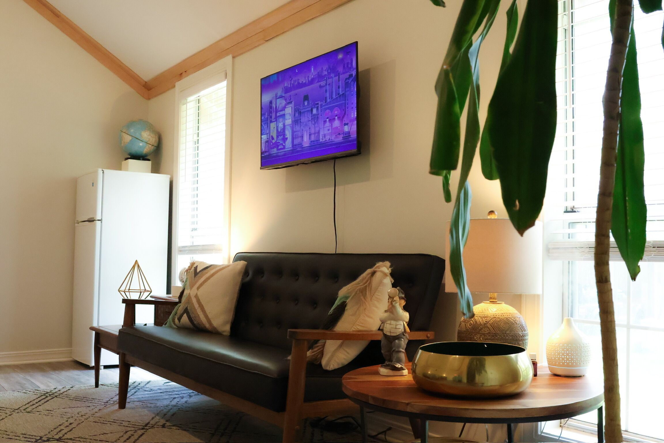 A living room with a sofa, a television, a globe, a lamp, and a table with decorative items.