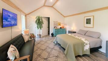 A bedroom with a bed, a sofa, a TV, a ceiling fan, and a door leading to another room.