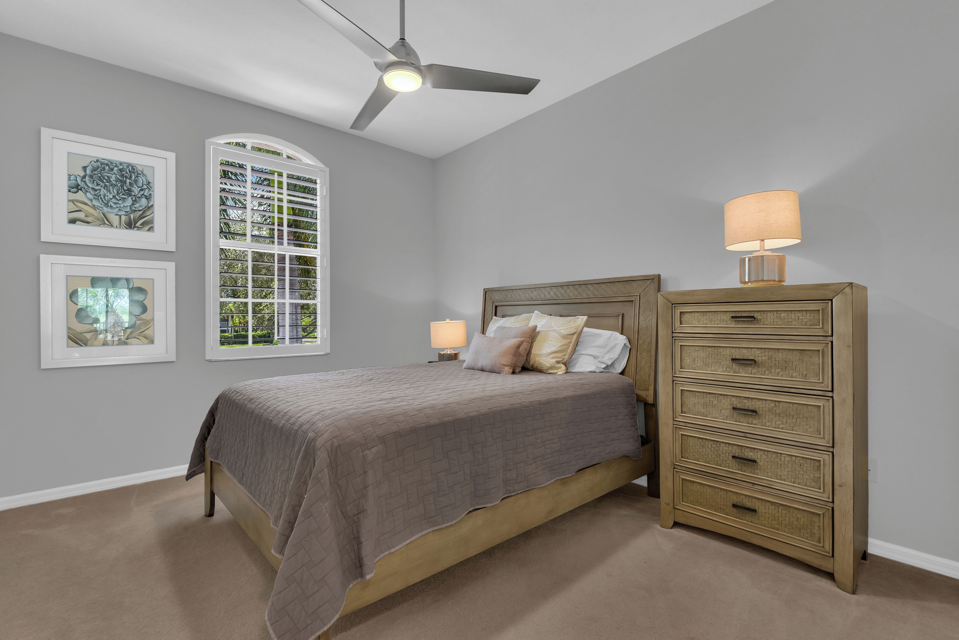 Une chambre à coucher comprenant un lit, une commode, un ventilateur de plafond et des œuvres d’art encadrées accrochées au mur.