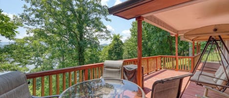 A covered deck with outdoor furniture, a swing chair, and a glass table.