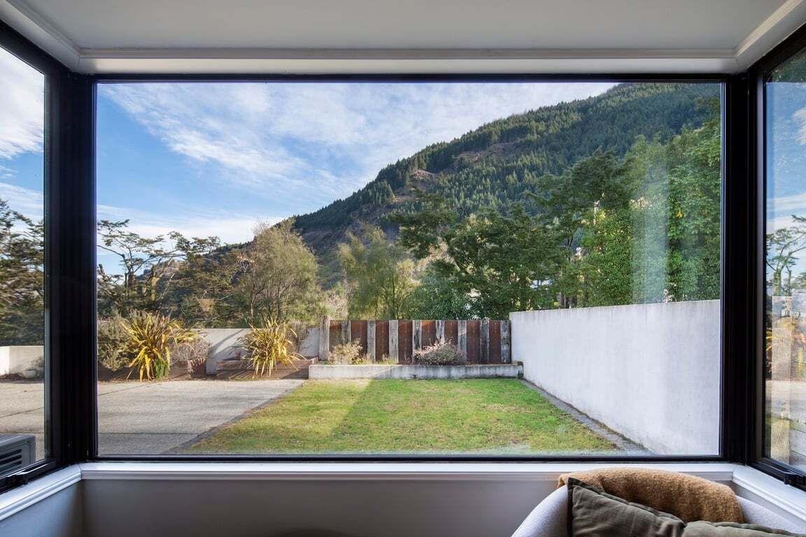 A room with a large window overlooking a well-maintained garden and a mountain.