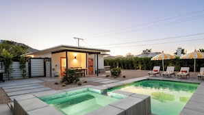 Et moderne hus med pool, udendørs møbler og en overdækket terrasse.