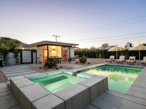 Ein modernes Haus mit Pool, Sitzgelegenheiten im Freien und einer überdachten Terrasse.