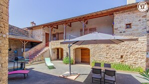 Un edificio de piedra con un porche cubierto, mobiliario exterior y una escalera.