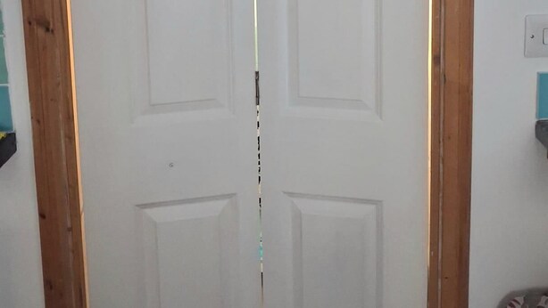 A room with a wooden-framed door, a white wall, and a hanging garment rack with a white hanger.