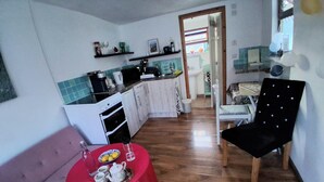 A compact kitchen with a refrigerator, stove, and sink. A dining area with a table set for tea and a black upholstered chair.