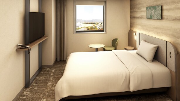 Quarto de hotel com cama, televisão presa à parede, janela com vista, mesa pequena e uma cadeira.