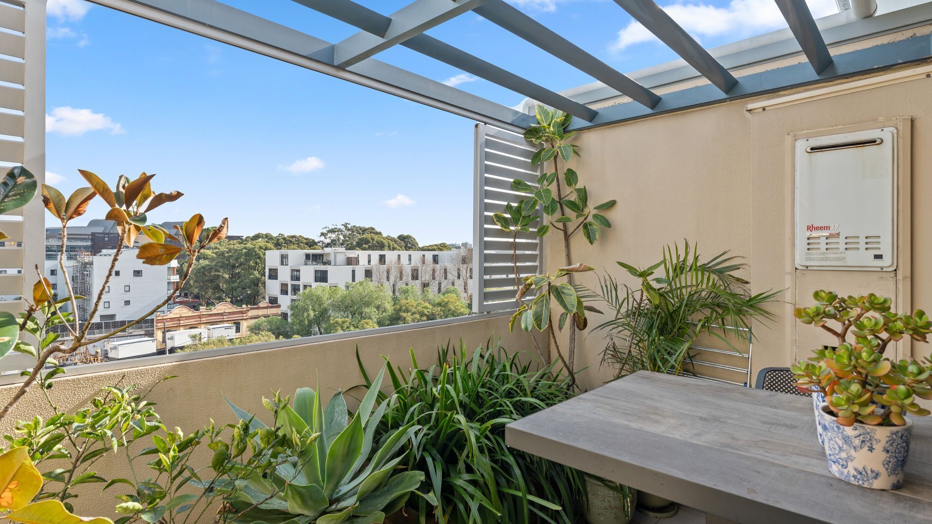 A balcony with a view of buildings, a table, and various plants.