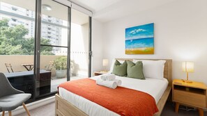 Ein Hotelzimmer mit Bett, Nachttisch, Stuhl, Tisch und Blick ins Freie.