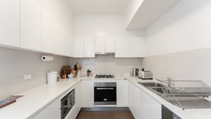 Eine moderne Küche mit weißen Schränken, einem Gasherd, einem Backofen, einer Spüle mit Geschirrgestell und einem Toaster.