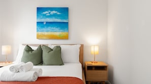 Ein Hotelzimmer mit einem Bett, Kissen, einem Nachttisch, Lampen und einem Bild mit einer Strandansicht.
