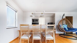Un comedor con una mesa y sillas de madera, un sillón colgante y una cocina al fondo.