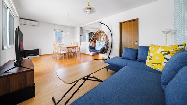 Una sala de estar moderna con un sofá azul, una silla colgante, una mesa de centro de madera y un televisor sobre un mueble de madera.