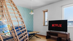 Una habitación con una silla colgante, un televisor mostrando 'NETFLIX' y una ventana.