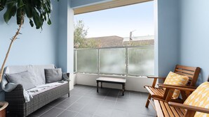 Ein Balkon mit einer Rattan-Couch, einem Holzstuhl, einem kleinen Tisch und einem Blumentopf.