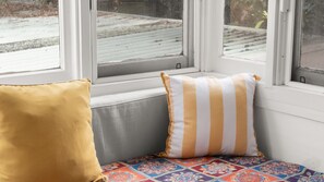 Ein Fensterplatz mit zwei Kissen, einem gemusterten Teppich und Blick auf eine verschneite Landschaft.