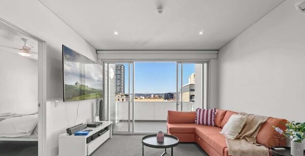 A modern hotel room with a balcony, a sofa, a coffee table, and a TV. - Central Adelaide 2BR Queen  2 Singles  WiFi (Adelaide)