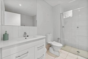 A modern bathroom with a white sink, mirror, toilet, and glass shower enclosure. - Central Adelaide 2BR Queen  2 Singles  WiFi (Adelaide)