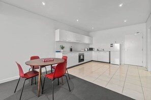 A modern kitchen with white cabinets, a dining table with red chairs, and a small island with a sink. - Central Adelaide 2BR Queen  2 Singles  WiFi (Adelaide)