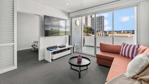 Ein modernes Wohnzimmer mit einer Couch, einem Couchtisch, einem Flachbildfernseher und einer Schiebeglastür, die auf einen Balkon mit Stadtblick führt.
